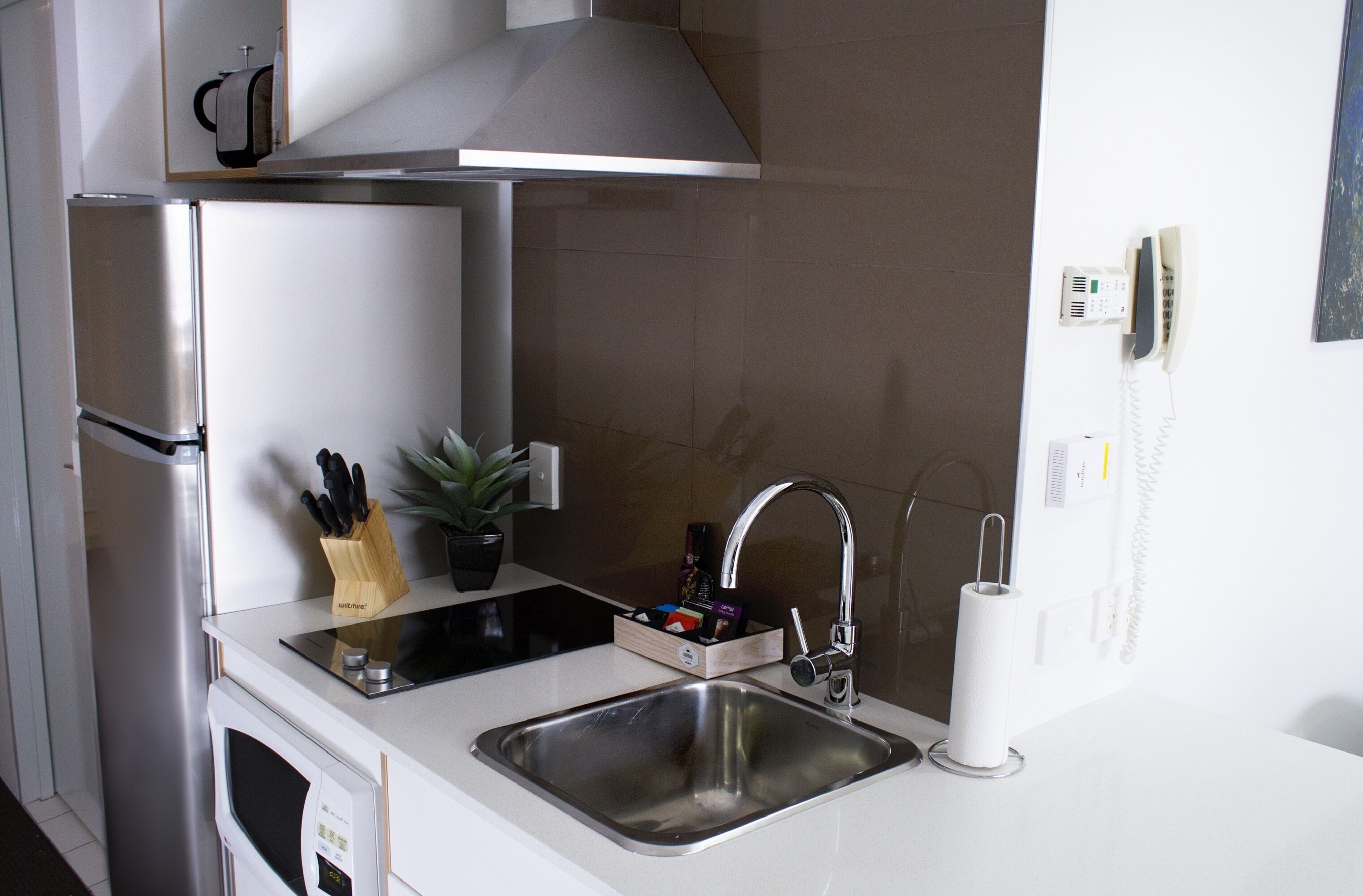 Eine kompakte Küche mit Edelstahl-Kühlschrank, Mikrowelle, Spüle mit modernem Wasserhahn und einem kleinen Topfpflanze.