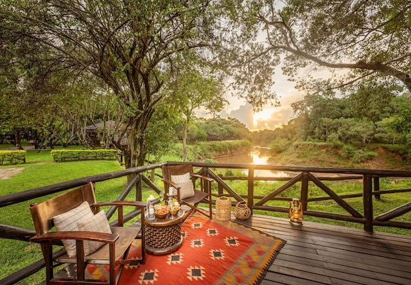 Una terraza de madera con vistas a un río, rodeada de abundante vegetación.