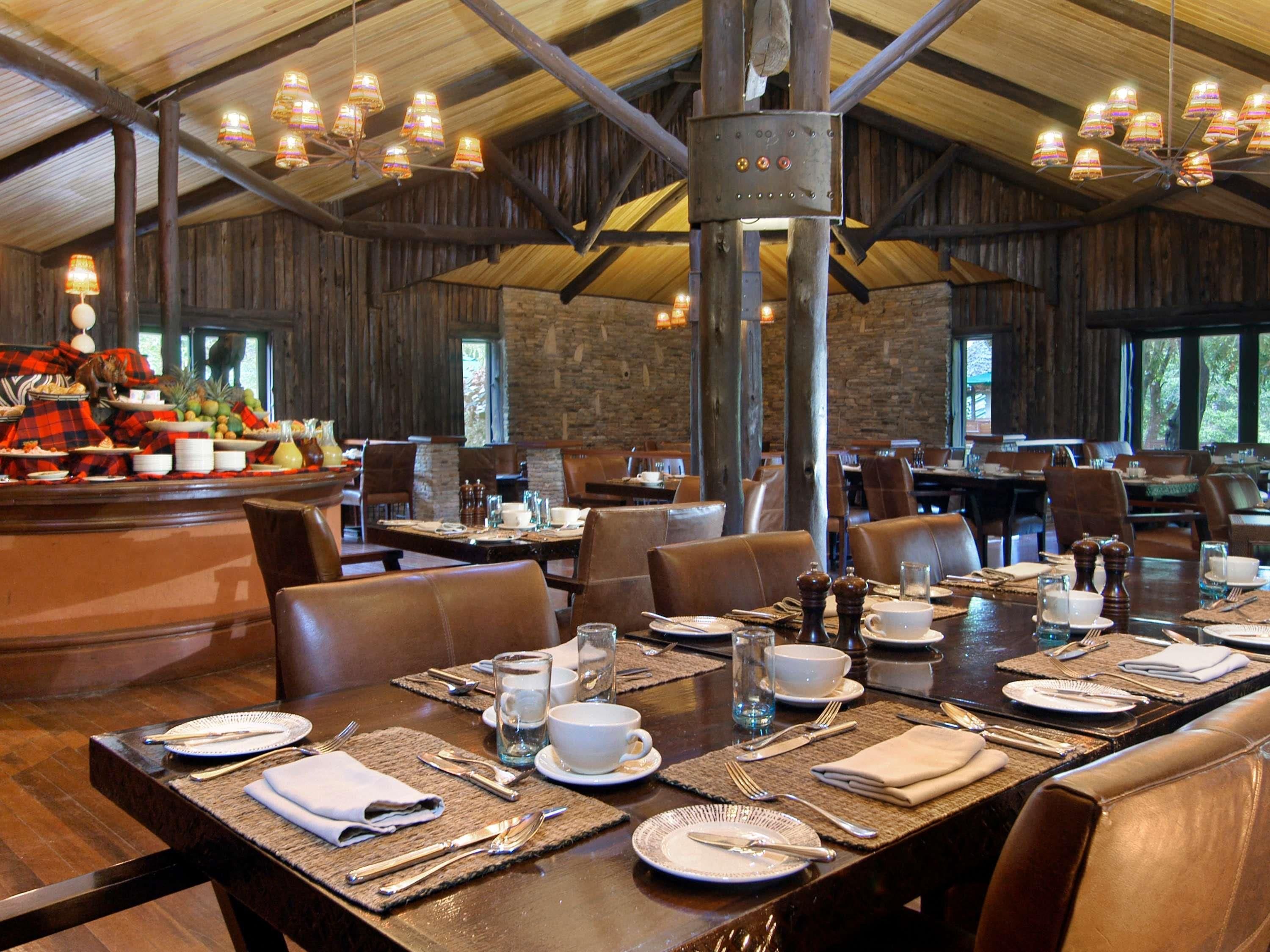 A dining area with wooden tables and chairs, a buffet with fruits and dishes, and a rustic interior with exposed beams and stone walls.