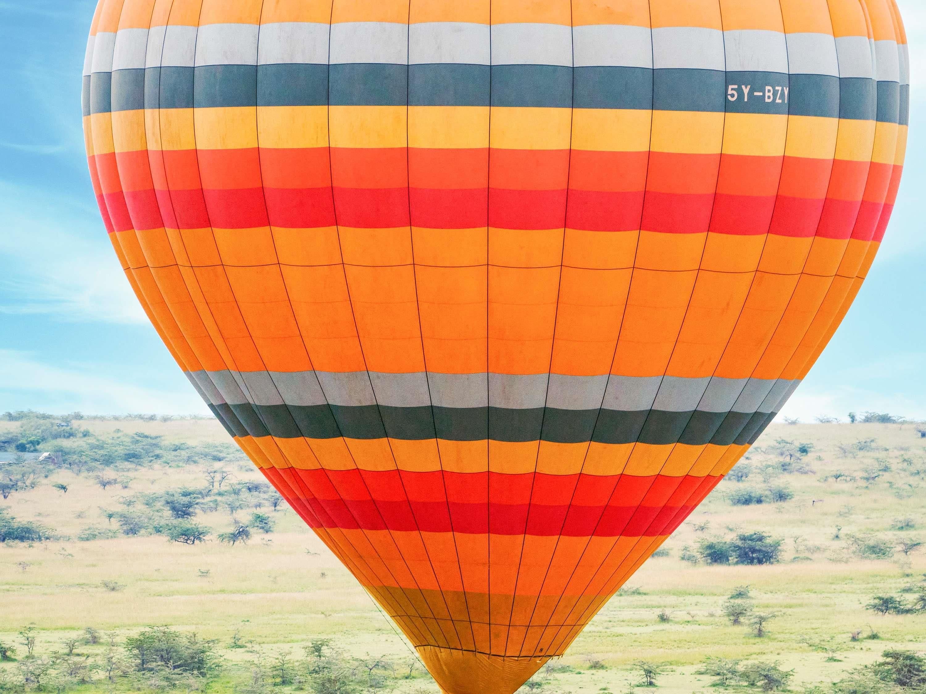Un globo aerostático con diseño a rayas y el número de registro '5Y-BZY' sobre un paisaje de fondo.