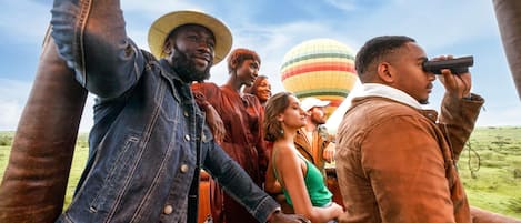 A group of people on a safari vehicle with a hot air balloon in the background.