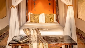 A bed with a canopy, patterned pillows, a bedside table with a book, and wall-mounted lamps. - Fairmont Mara Safari Club (Maasai Mara)