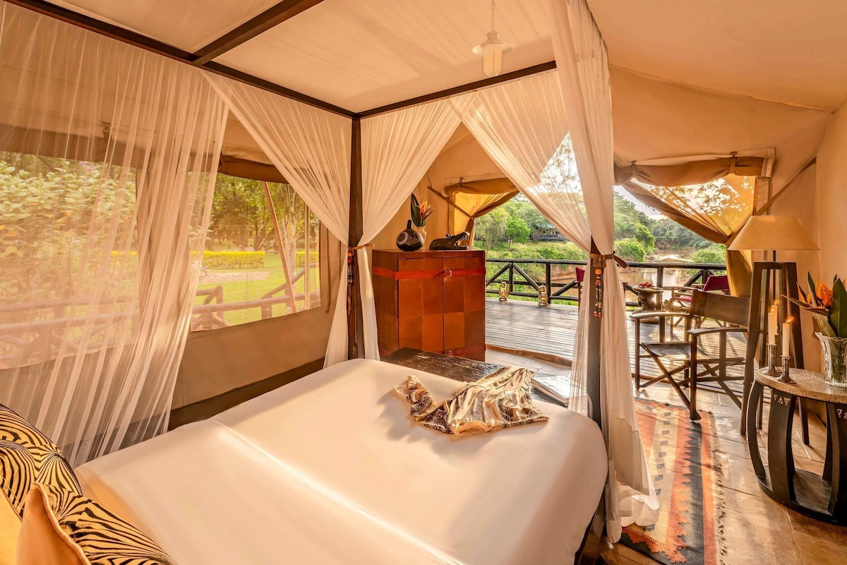 A tent-style room with a bed, a table with chairs, and a view of a garden.