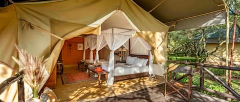 A tented accommodation with a bed, a table with a bowl of fruit, and a woven basket.