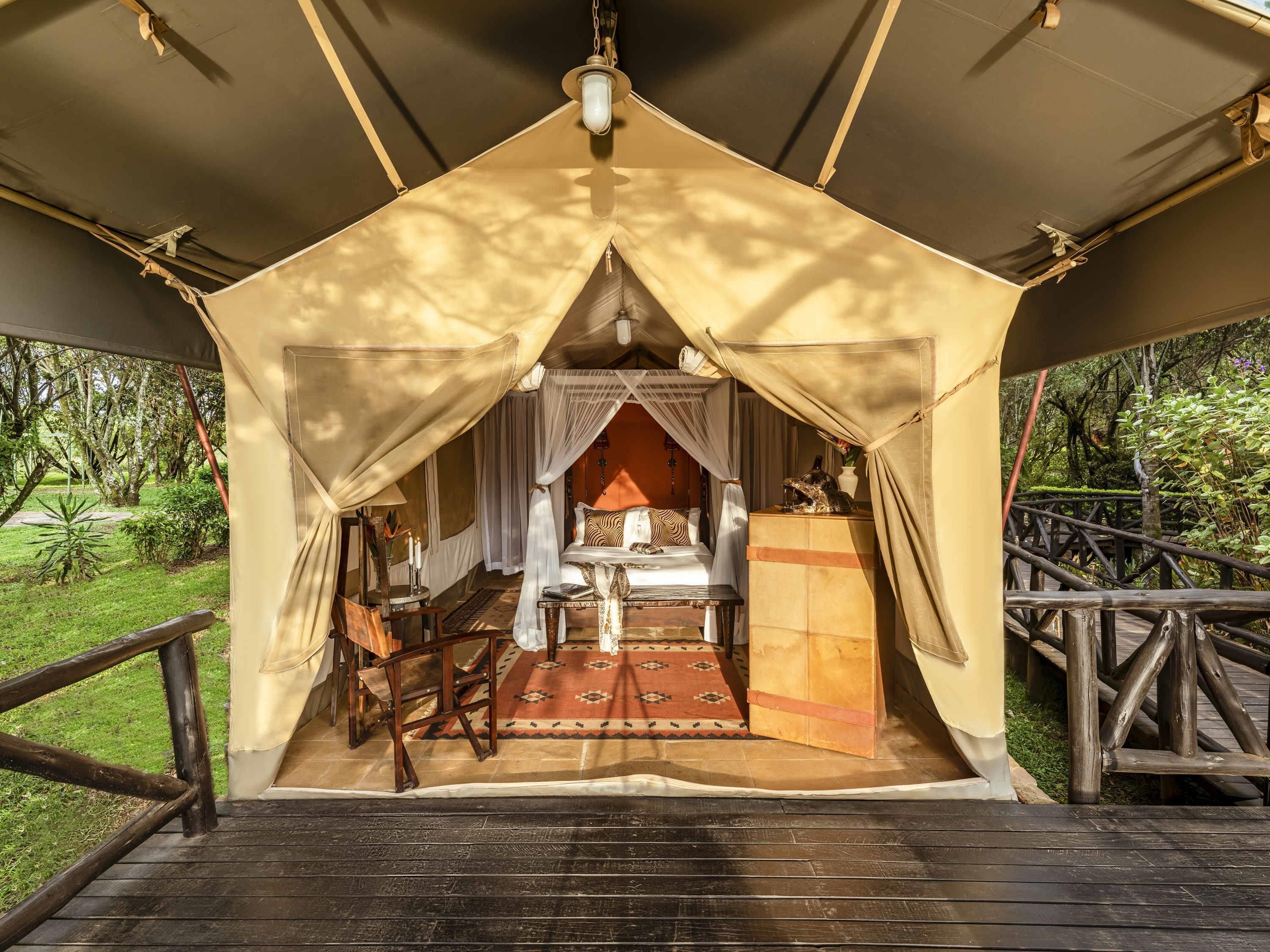 A tented accommodation with a bed, bedside table, and a view of the surrounding greenery.