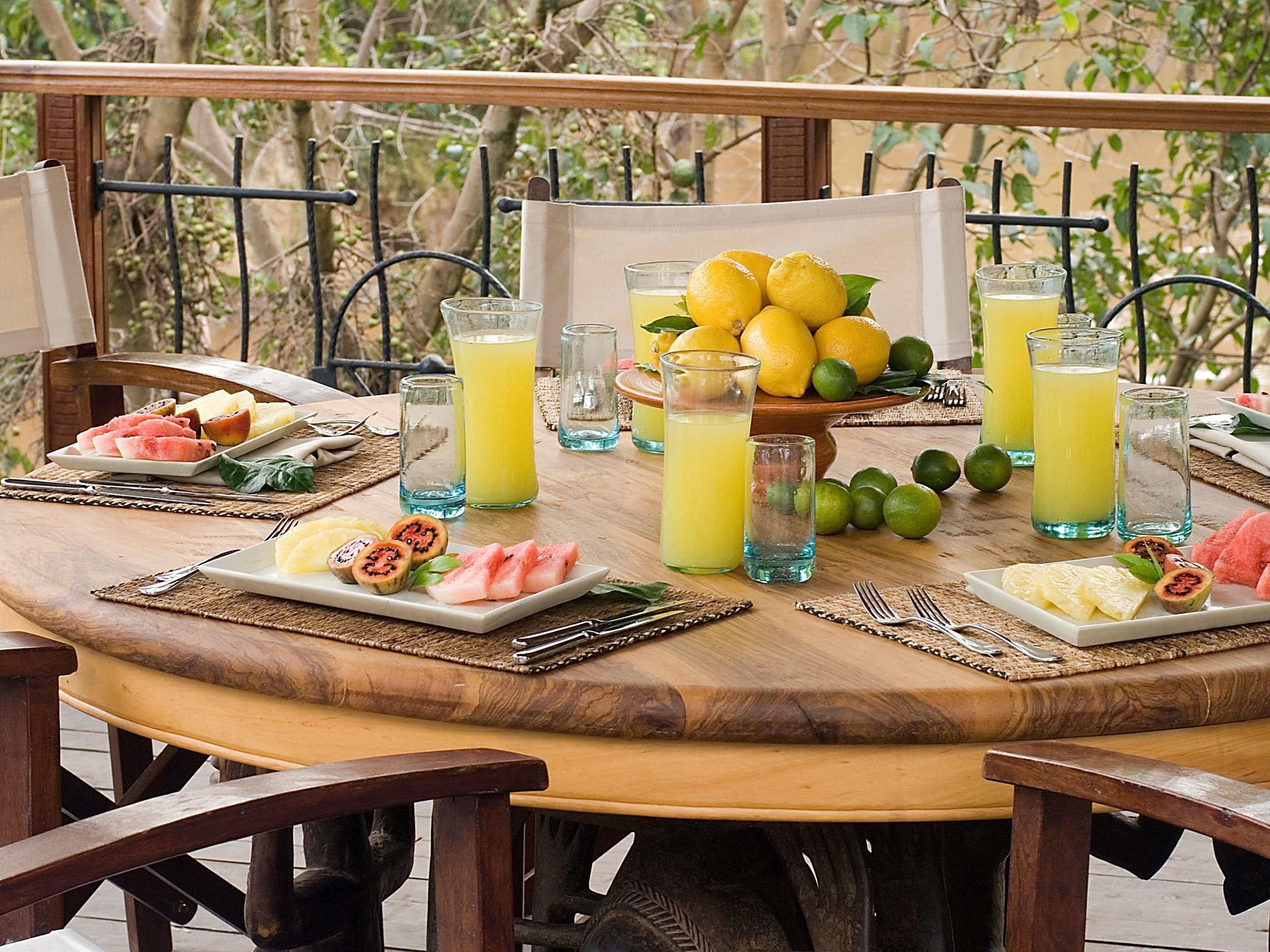 Une table ronde en bois, sur laquelle sont disposés divers fruits et boissons, entourée de chaises.