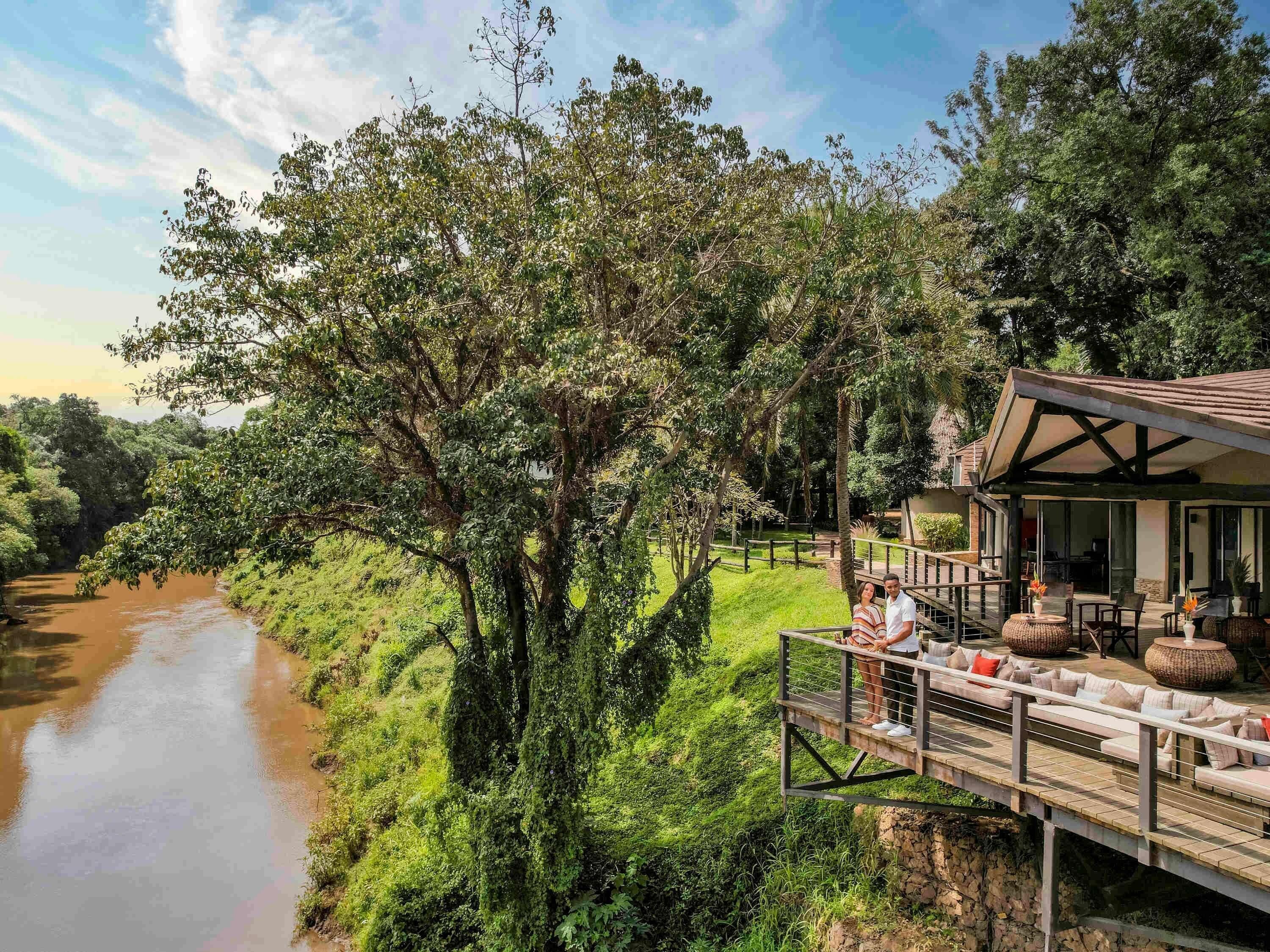A riverside property with a deck overlooking a river, surrounded by lush greenery.