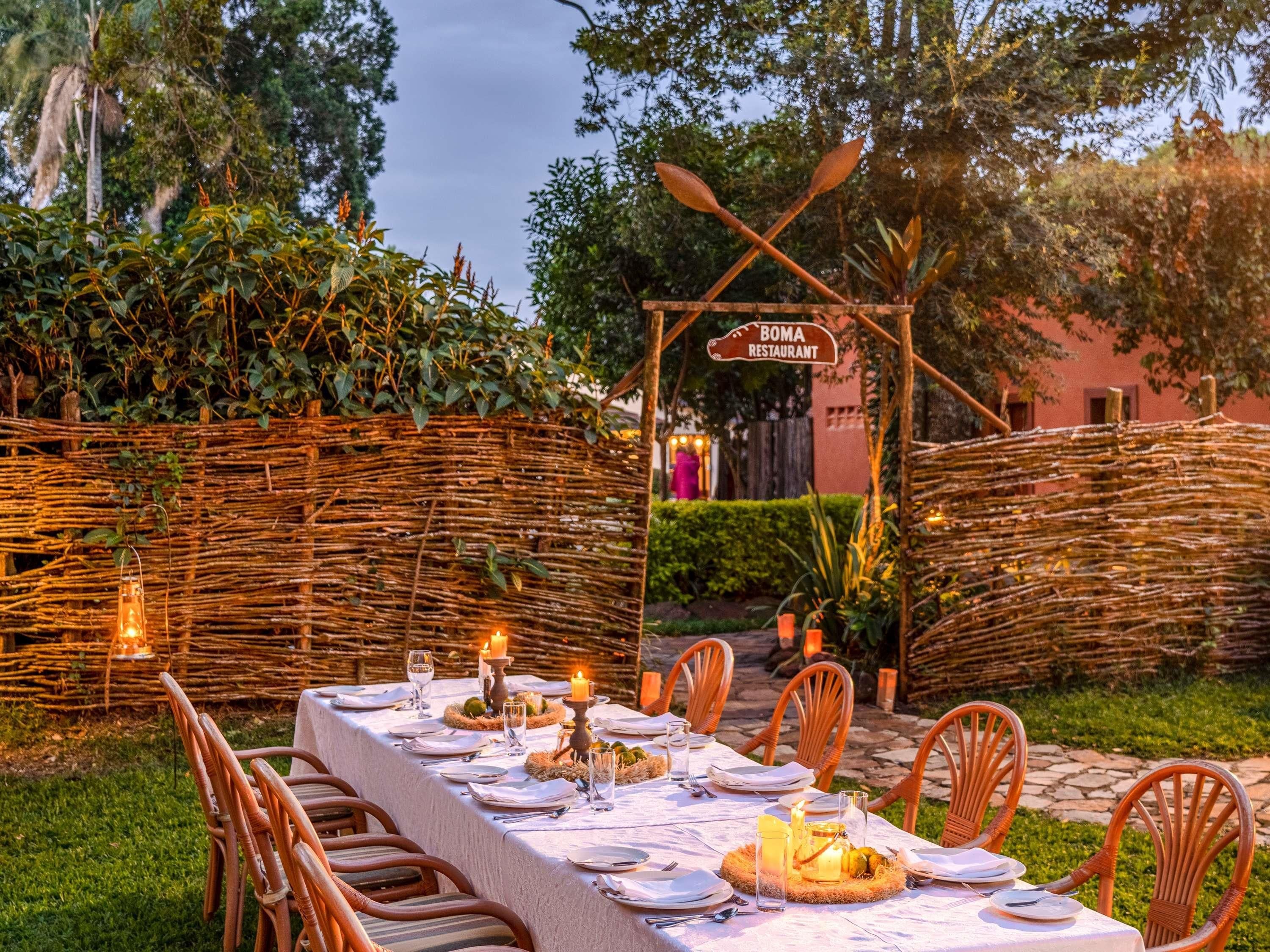 An outdoor dining setup with a table set for four, surrounded by wicker chairs, under a sign for Boma Restaurant.
