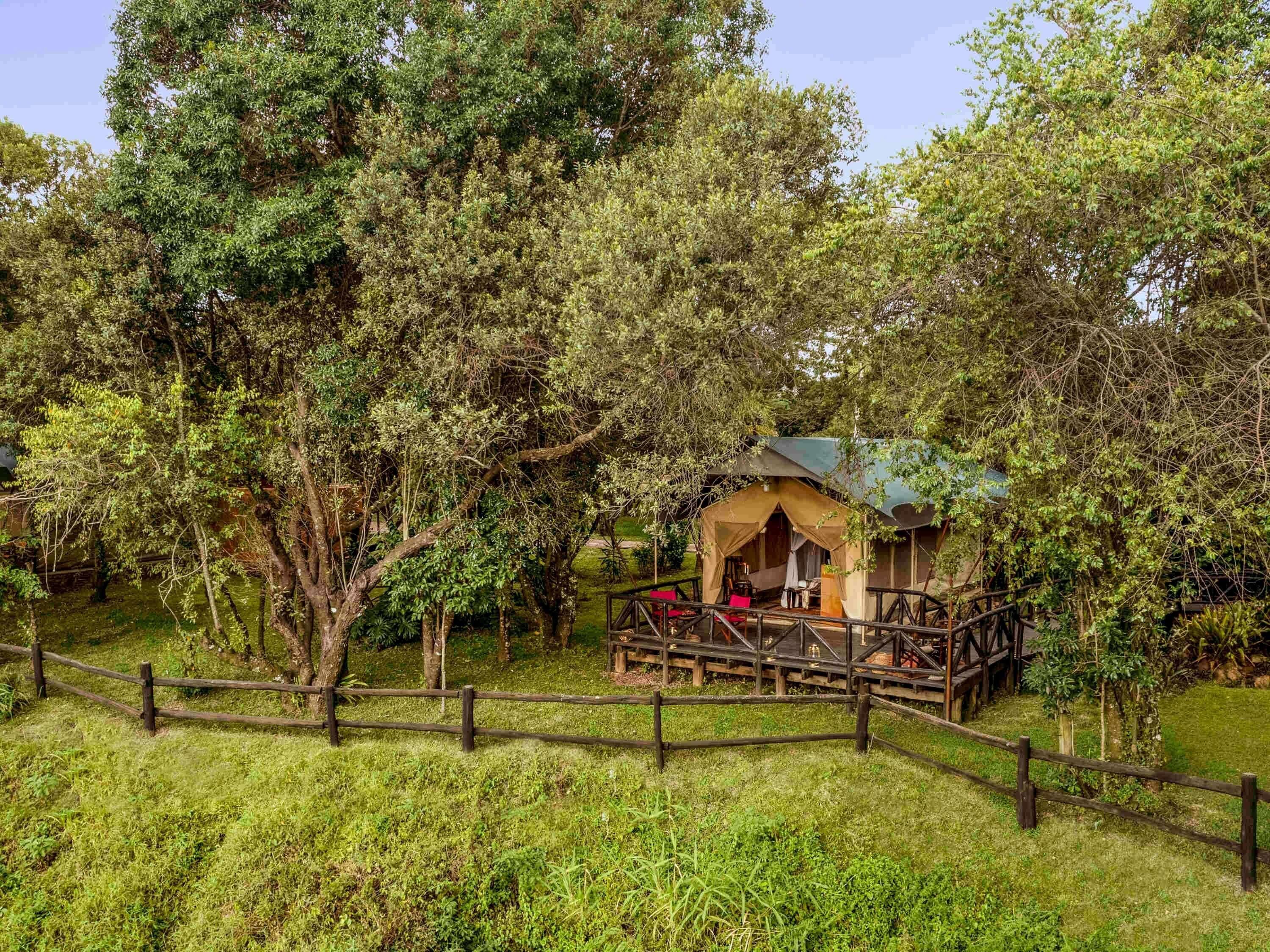 A rustic wooden cabin with a porch, surrounded by dense trees and a wooden fence.