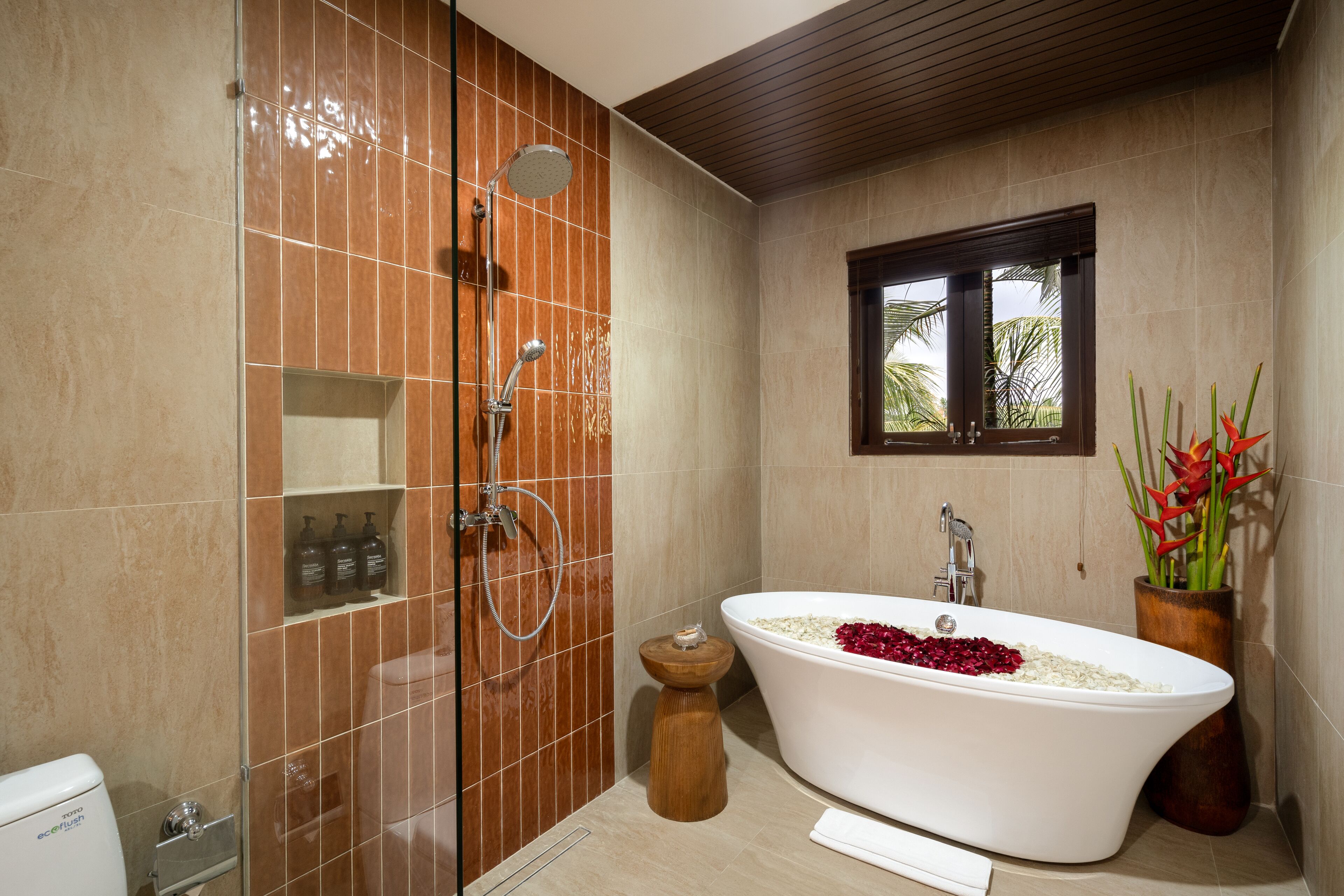 A modern bathroom with a freestanding bathtub, a shower enclosure, and a window with a view of palm trees.
