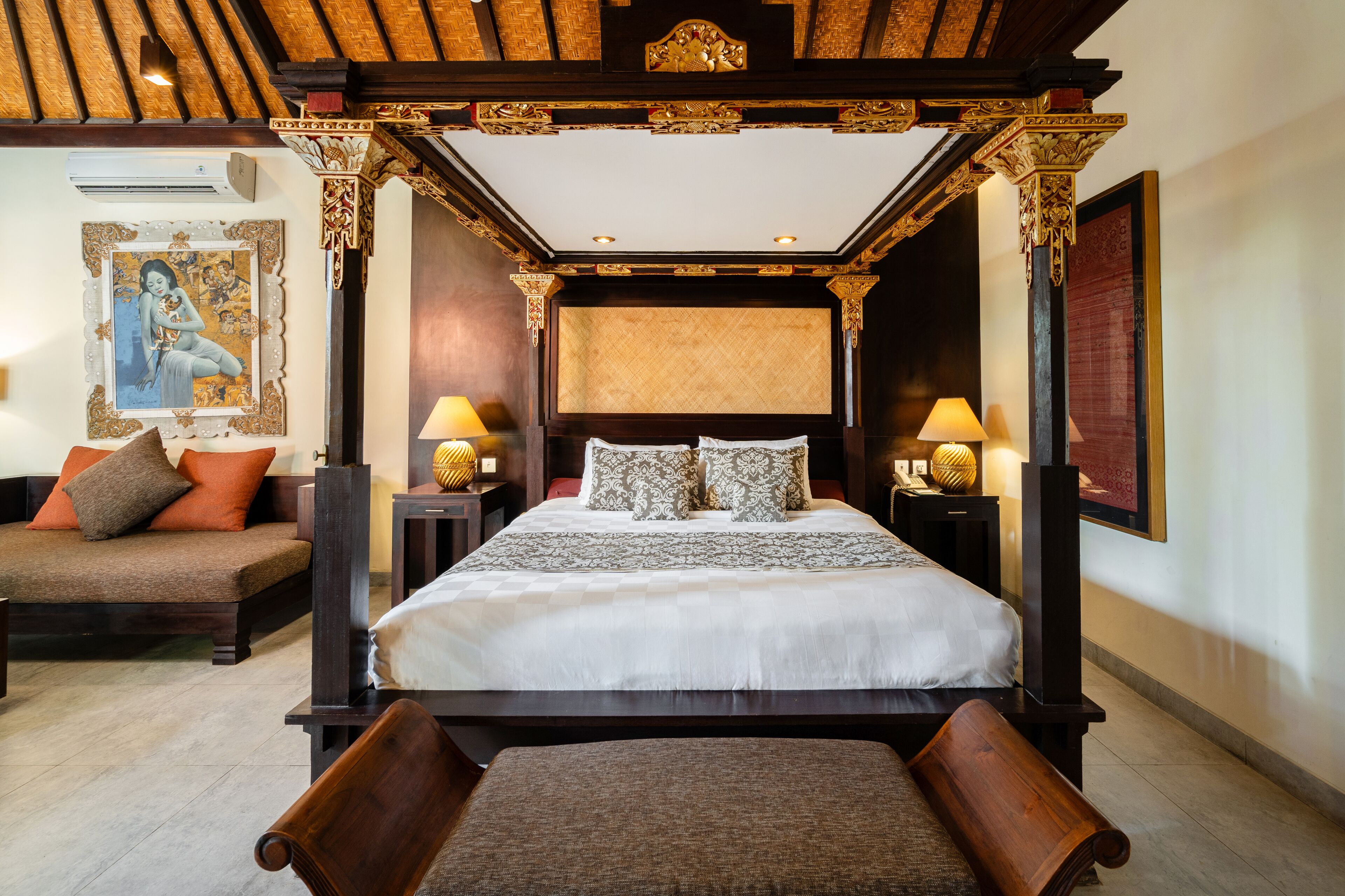 A four-poster bed with a canopy, a sofa, a bedside table with a lamp, and a wall-mounted air conditioner.