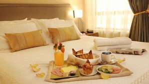 Una cama bien hecha con una bandeja de desayuno que incluye tostadas, fruta y una bebida.