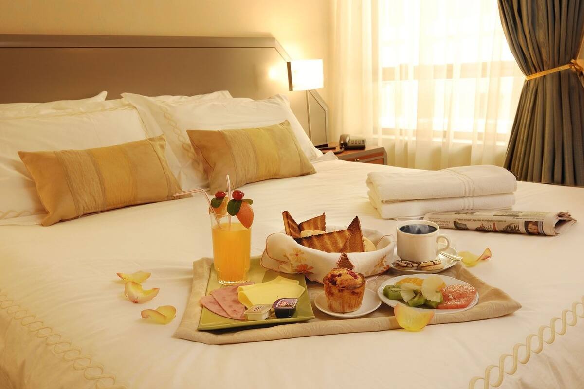 Una cama bien hecha con una bandeja de desayuno que incluye tostadas, fruta y una bebida.
