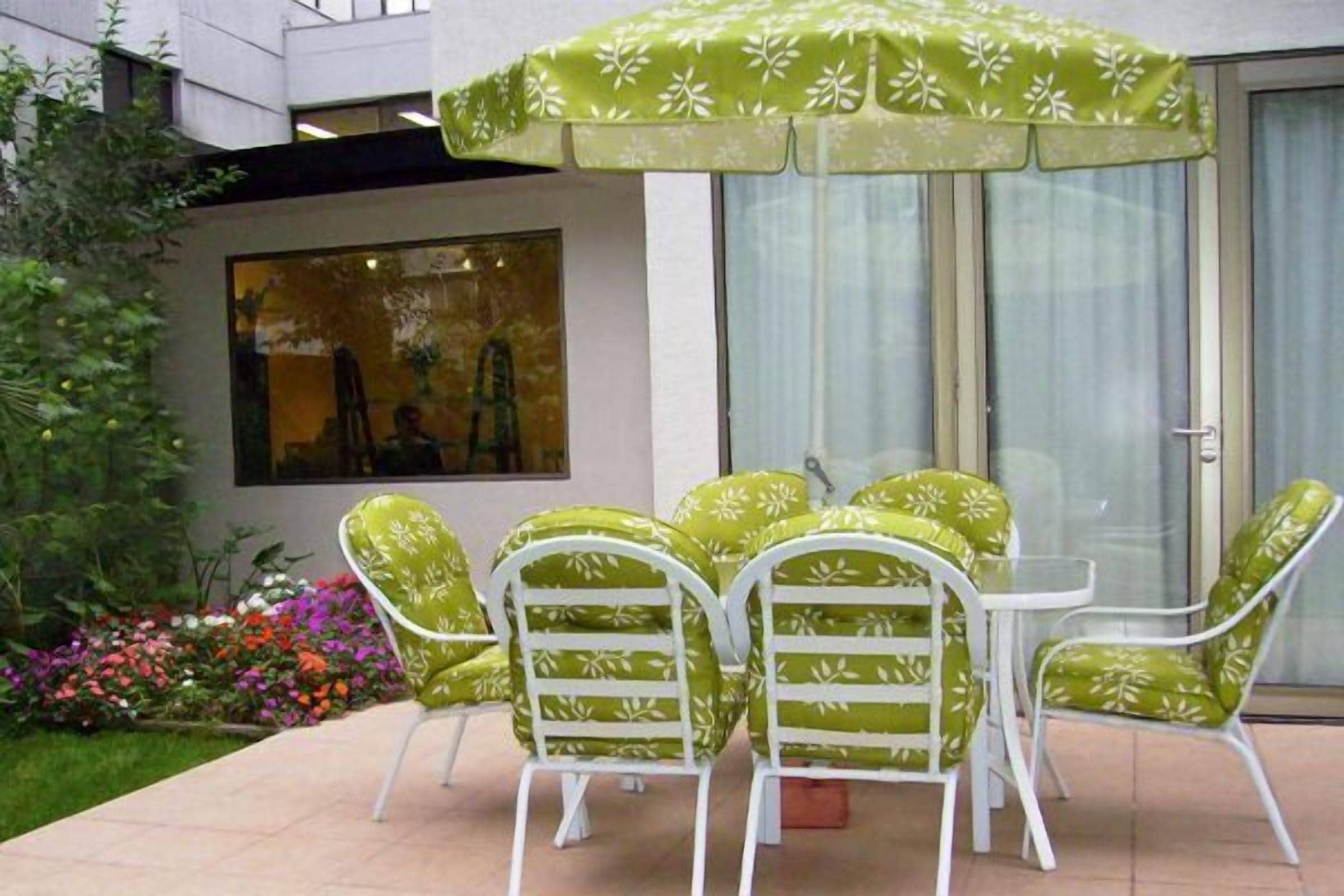 A patio with a glass door, green patterned chairs, and a white table.