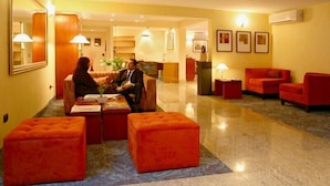 Un vestíbulo de hotel con una recepción, asientos rojos y un espejo grande.