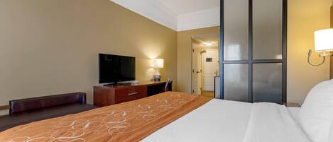 Habitación de hotel con cama, televisor, escritorio con lámpara y puerta que da a un baño.