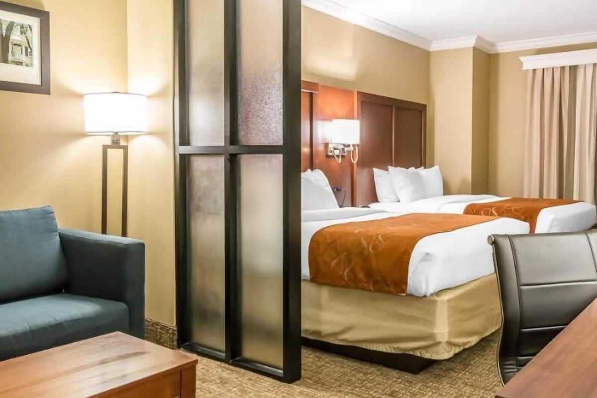 A hotel room with a sofa, a bed with two pillows, a nightstand, and a lamp.