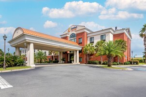 Un hotel Comfort Suites con entrada cubierta, palmeras y cielo despejado.