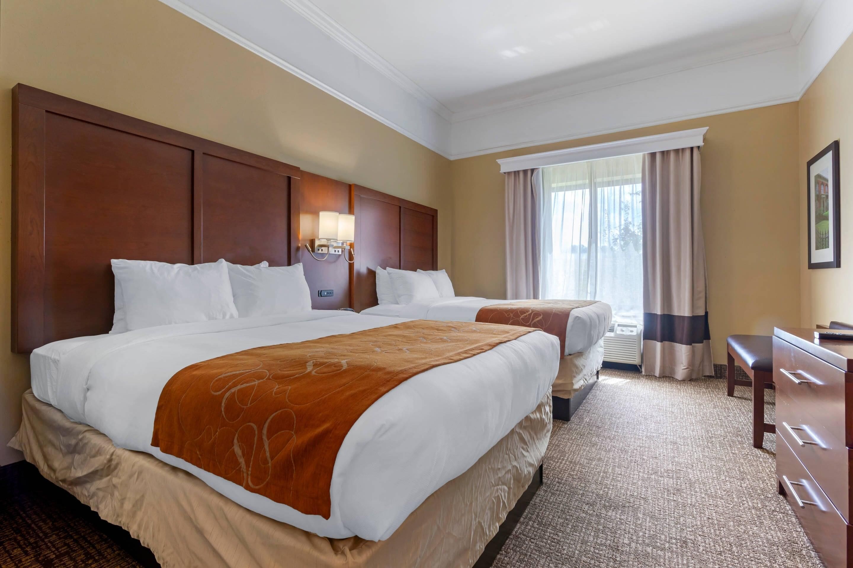 Habitación de hotel con dos camas, un escritorio y un ventanal con cortinas.