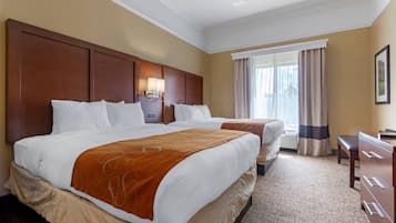 Habitación de hotel con dos camas, un escritorio y un ventanal con cortinas.