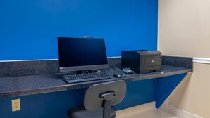 Un escritorio con una laptop, una computadora de escritorio e impresora frente a una pared azul.