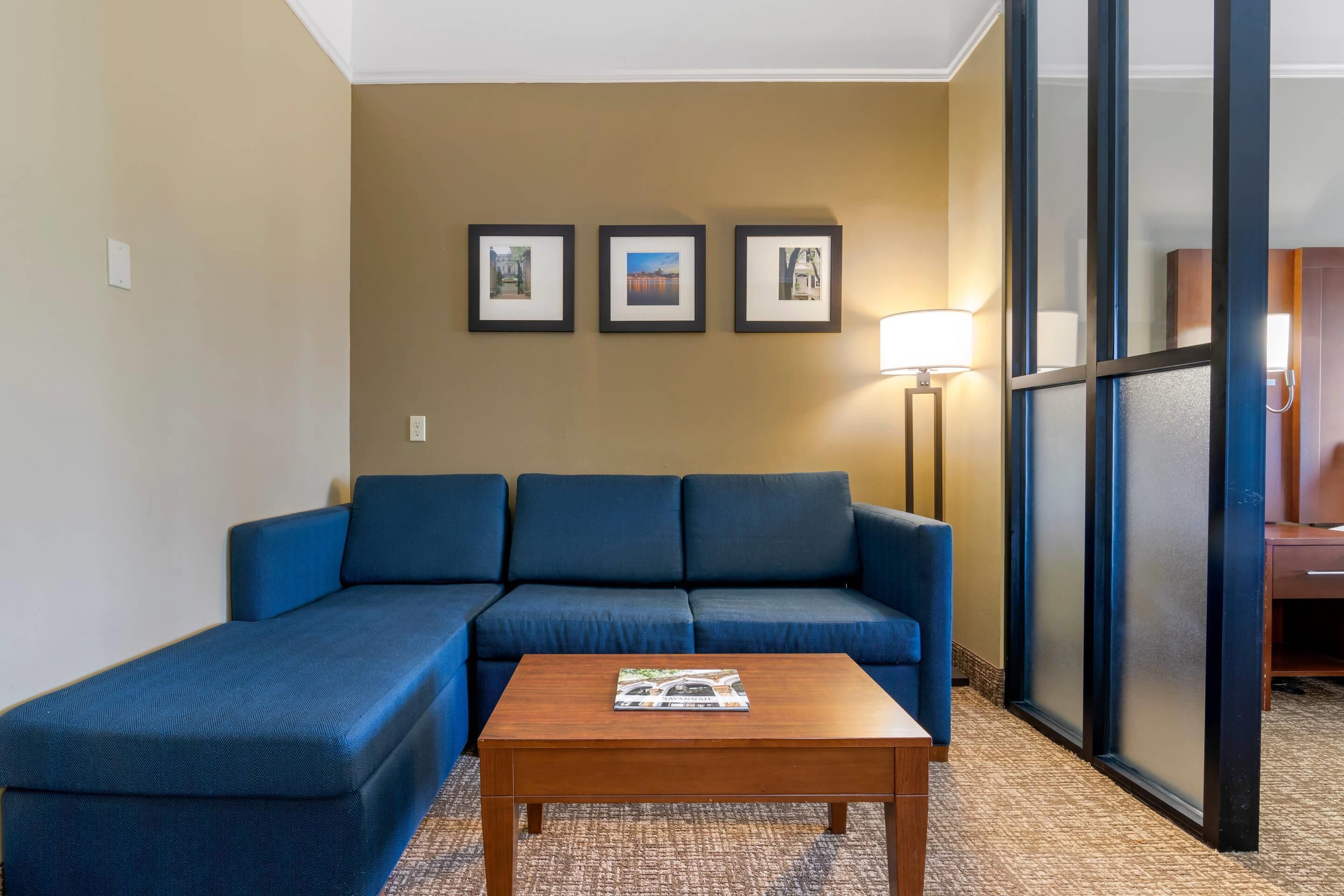 Habitación de hotel con sofá azul, una mesa de centro de madera y tres cuadros en la pared.