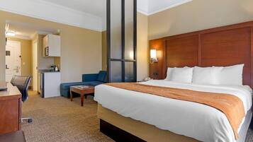 A hotel room with a large bed, a desk, a chair, a sofa, a coffee machine, and a minibar.