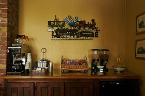 Zona de bar con una máquina de café, una cesta de aperitivos y una exposición de carteles antiguos de trenes en la pared.
