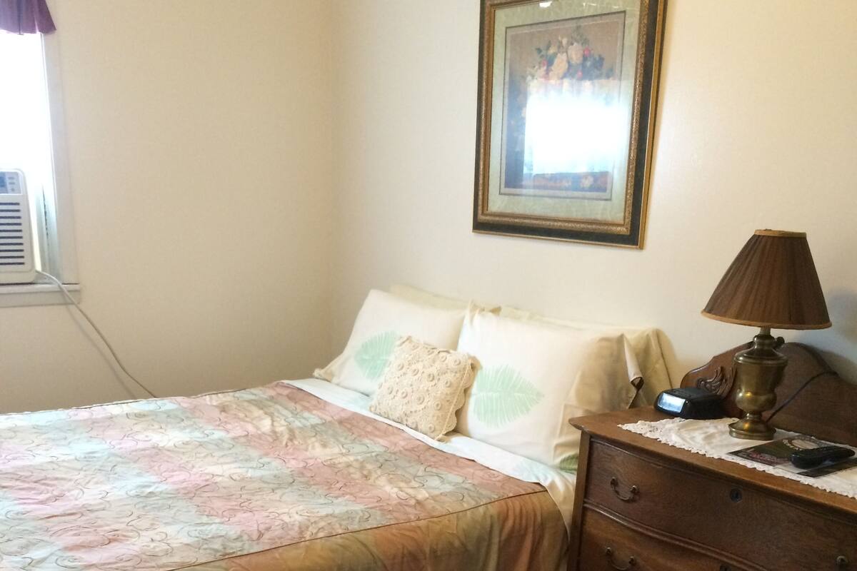 Une chambre à coucher avec un lit, une table de chevet, une lampe, une commode et un tableau encadré au mur.