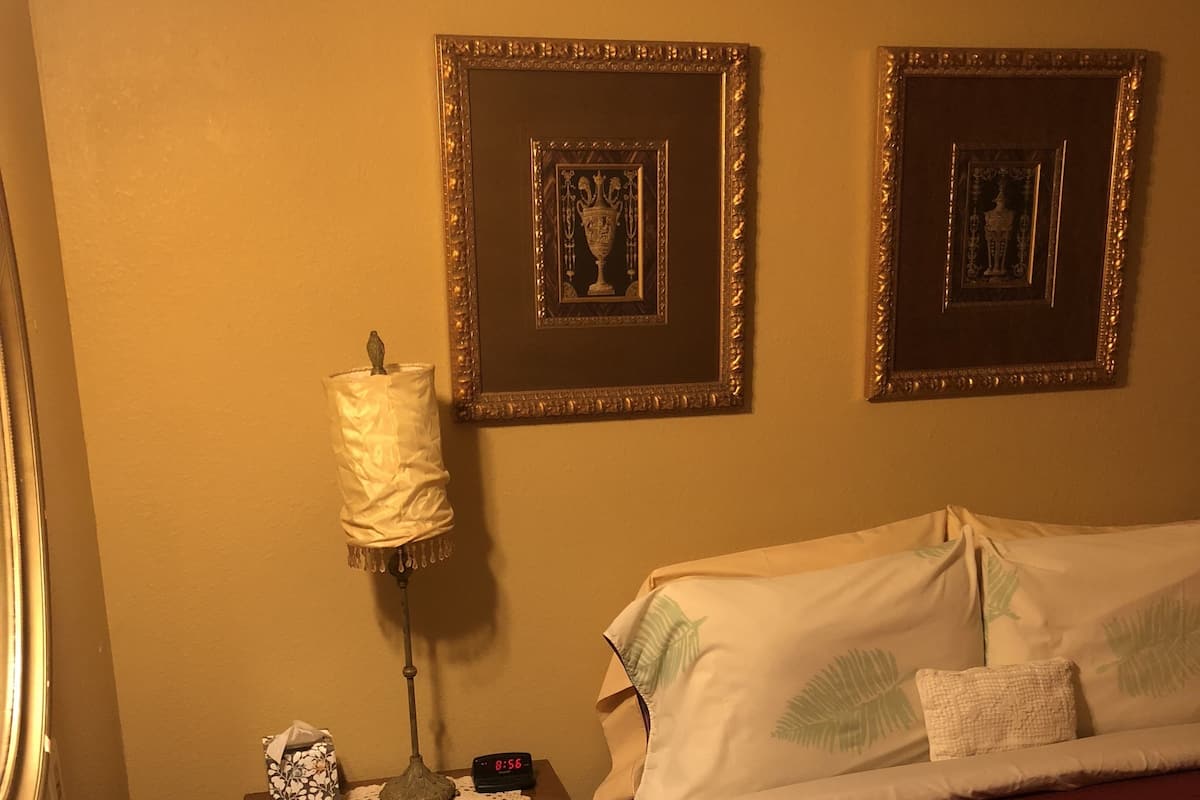 Une chambre d’hôtel comprenant un lit, une table de chevet avec une lampe, une horloge numérique et une salle de bain avec un lavabo et un miroir.
