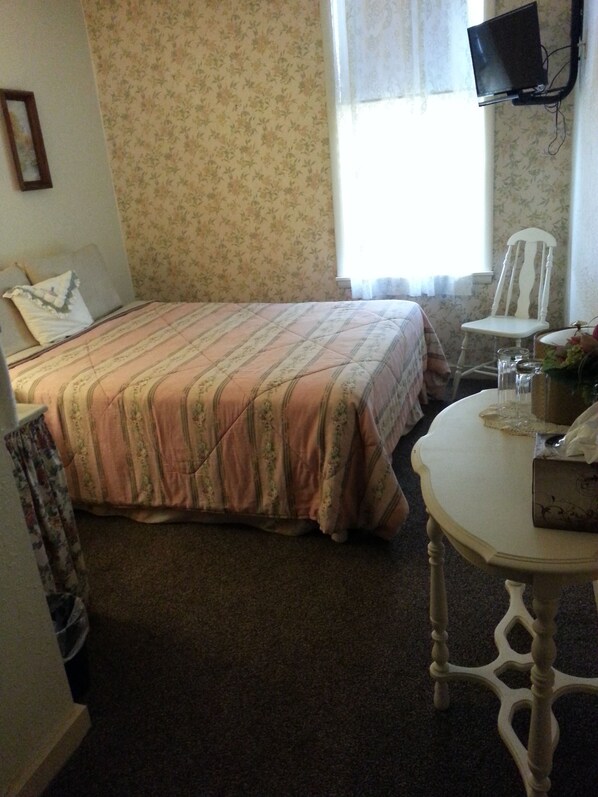 A bedroom with a bed, a chair, a table, and a television.