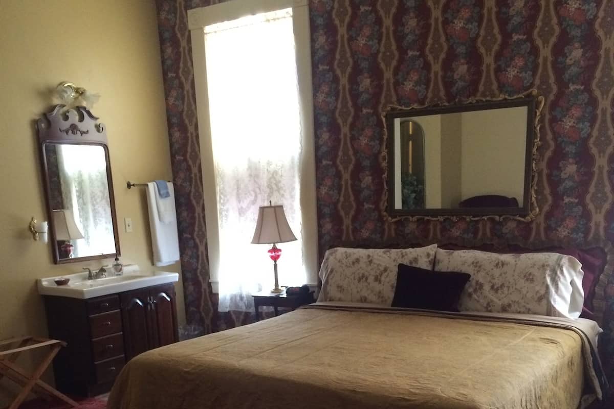 Une chambre à coucher avec un grand lit, une commode, un miroir et une fenêtre avec des rideaux.
