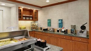 A hotel kitchen with buffet counters, wooden cabinets, and various appliances like a waffle maker and coffee machine. - Homewood Suites by Hilton Allentown-Bethlehem Airport (Bethlehem)