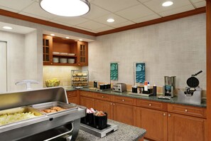 Eine Hotelküche mit Büfettstationen, Holzschränken und verschiedenen Geräten, darunter ein Waffelautomat und eine Kaffeemaschine.