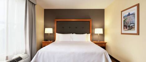 A hotel room with a large bed, two bedside lamps, a ceiling fan, a radiator, and a framed picture on the wall.
