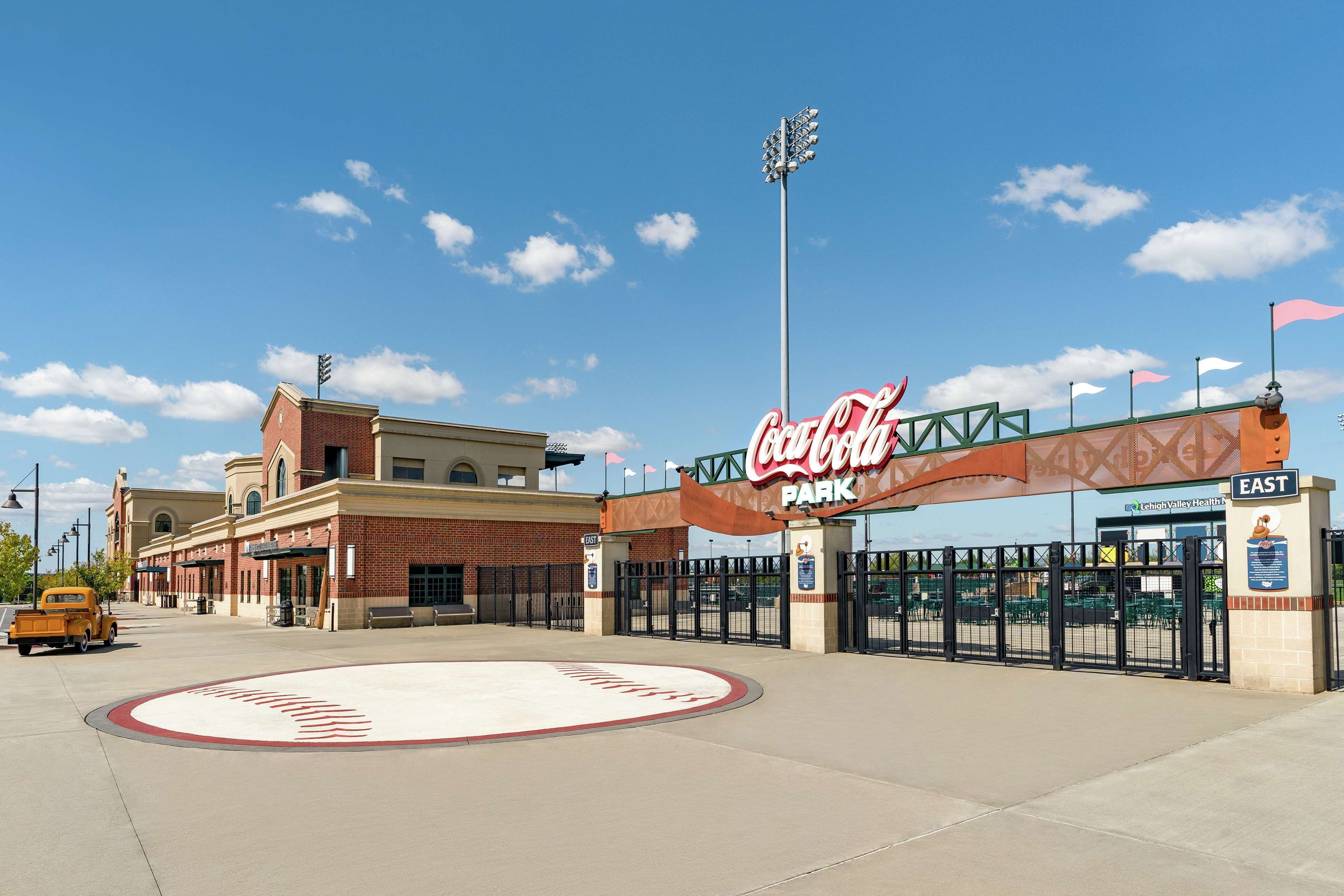 Entrada al Coca-Cola Park con un edificio de ladrillo, un campo de béisbol y un coche antiguo.