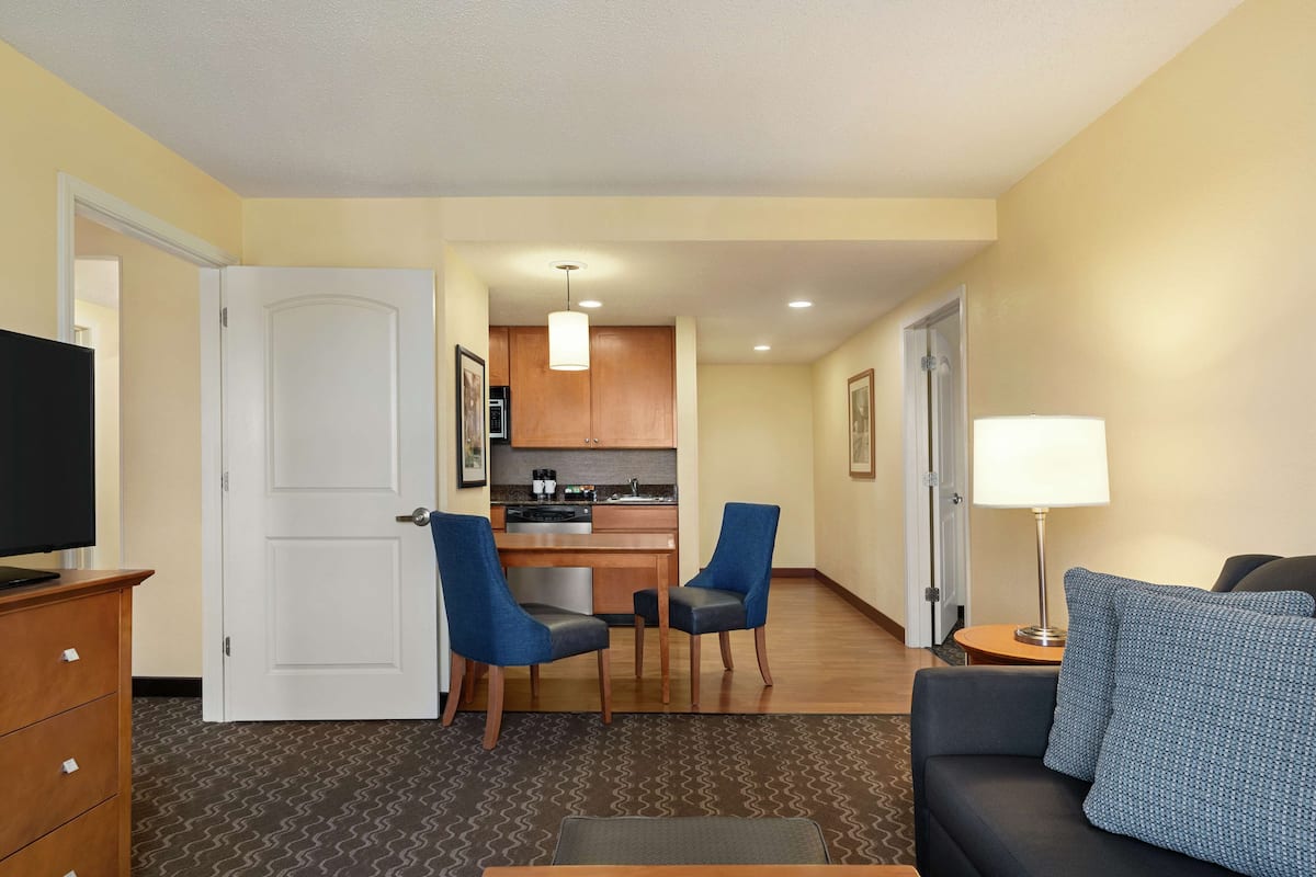 A hotel room with a living area, kitchenette, and a door leading to a bathroom.