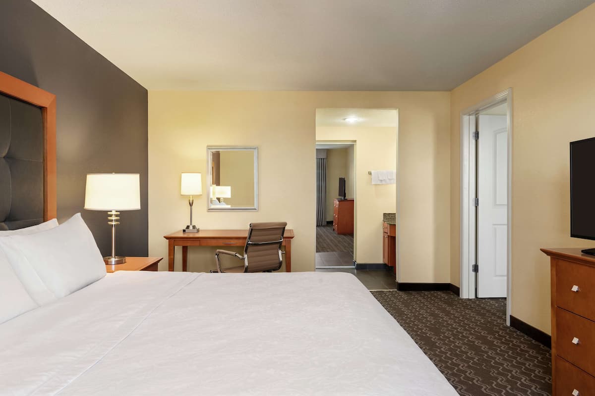 A hotel room with a large bed, a desk, a chair, a television, and a bathroom visible through an open door.