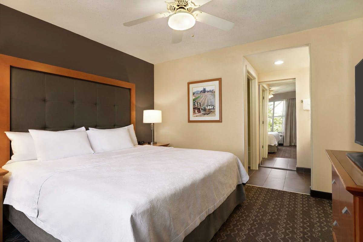 A hotel room with a large bed, a ceiling fan, a nightstand with a lamp, and a framed picture on the wall.