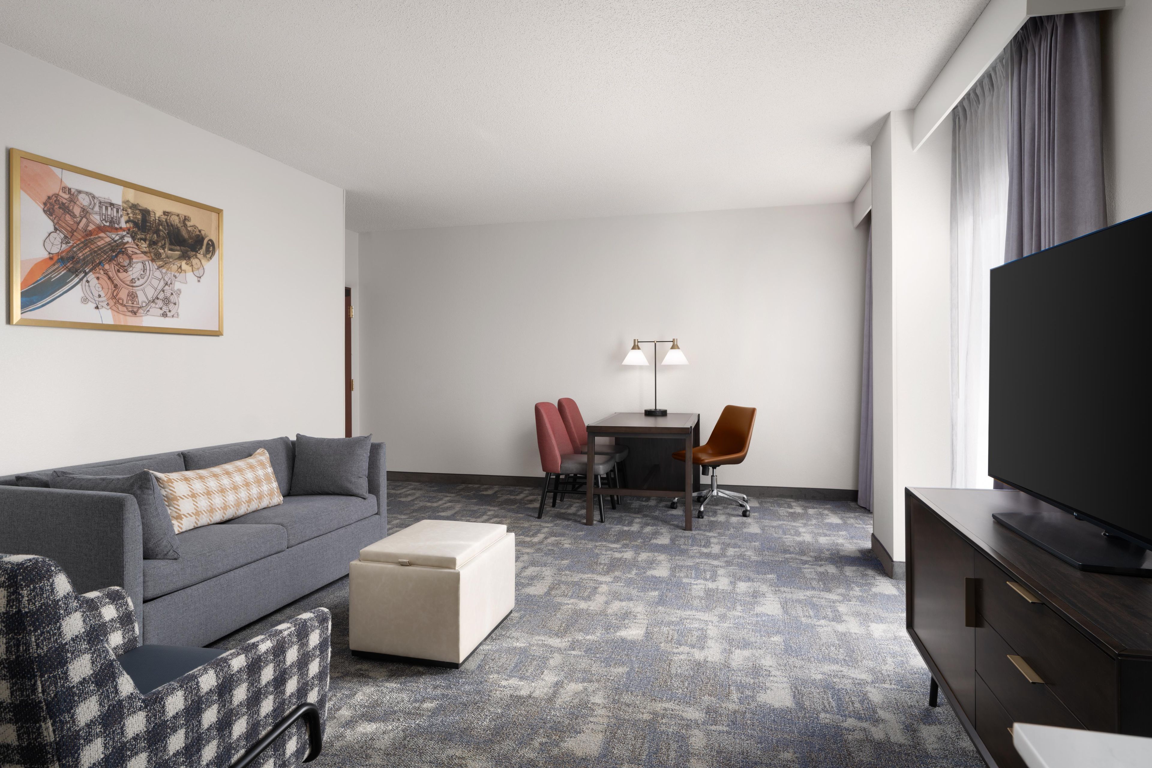 A hotel room with a gray sofa, a small table with two chairs, a television, and a painting on the wall.