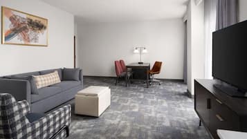 A hotel room with a gray sofa, a small table with two chairs, a television, and a painting on the wall.