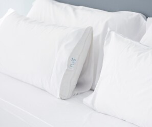 Ein Bett mit weißer Bettwäsche und Kissen, eines davon trägt ein 'Pure'-Logo.