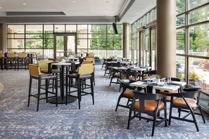 Un vaste espace de restauration intérieur, doté de nombreuses tables et chaises, de grandes fenêtres offrant une vue sur l’extérieur et d’un tapis à motifs.