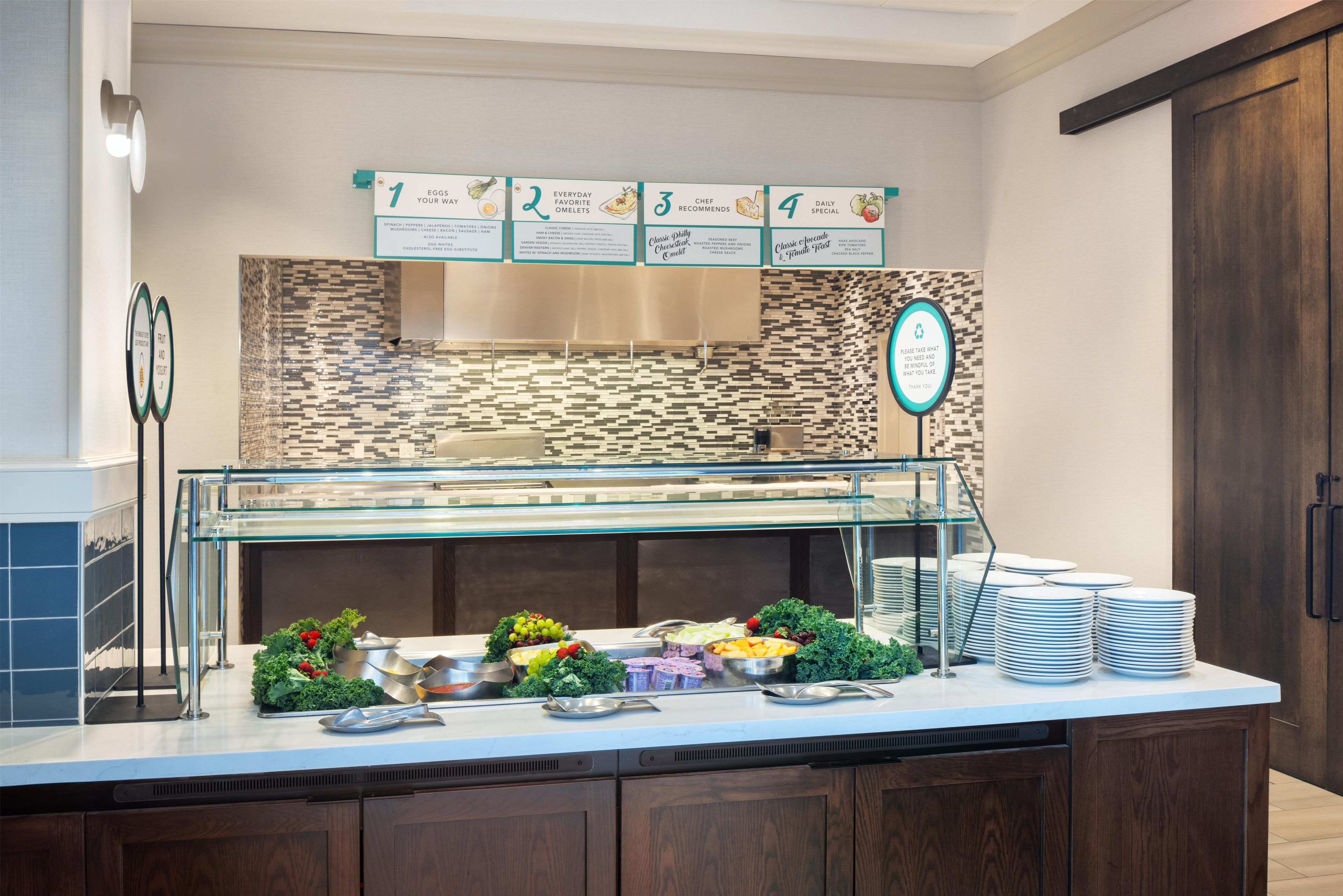 A buffet area with labeled signs for food options, a glass display case, and stacked plates.