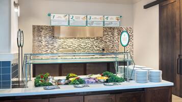 A buffet area with labeled signs for food options, a glass display case, and stacked plates.