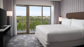 A hotel room with a large bed, a TV, a desk, and a balcony with a view.