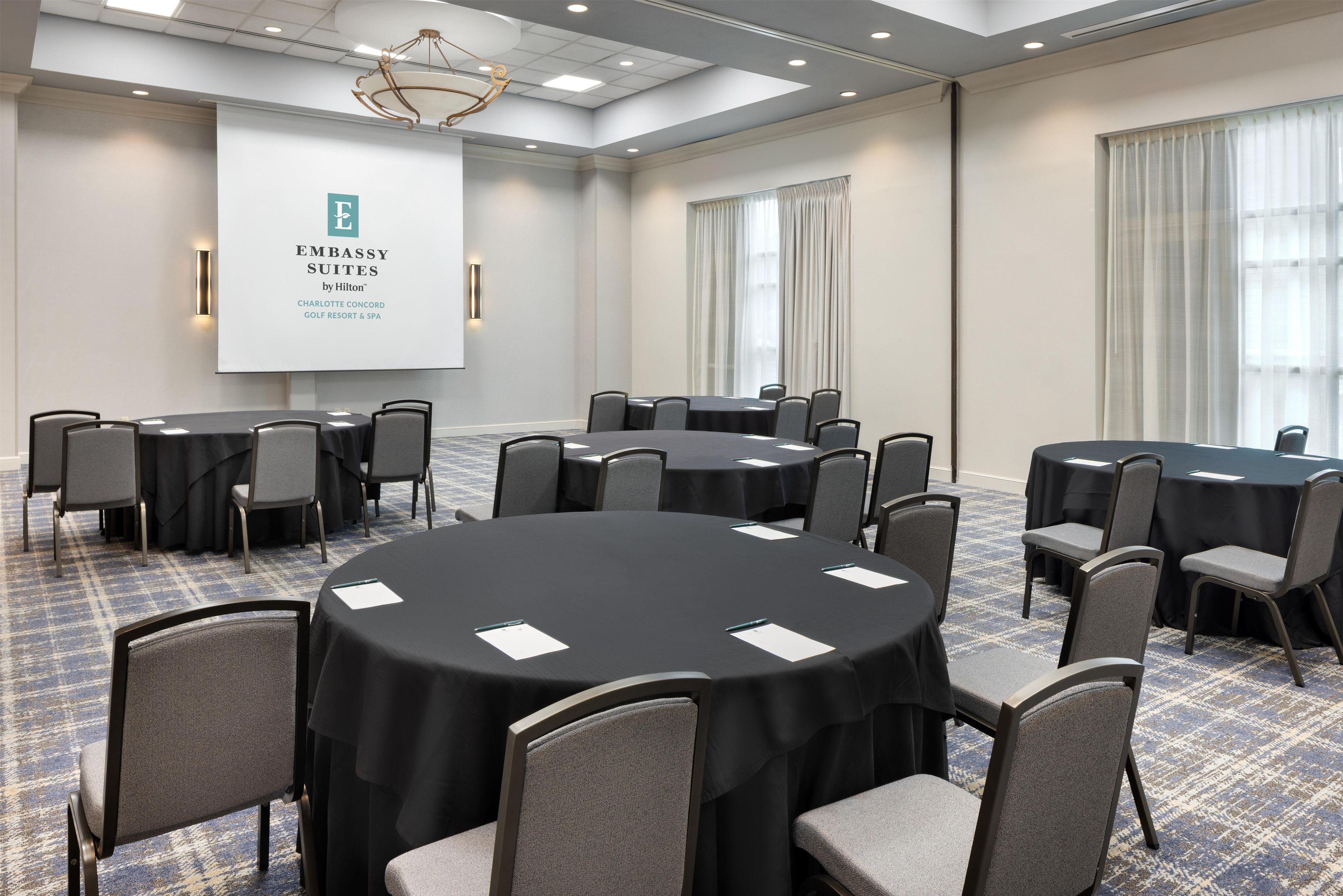 A conference room with round tables and chairs, a projector screen, and a chandelier.