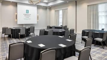 A conference room with round tables and chairs, a projector screen, and a chandelier.