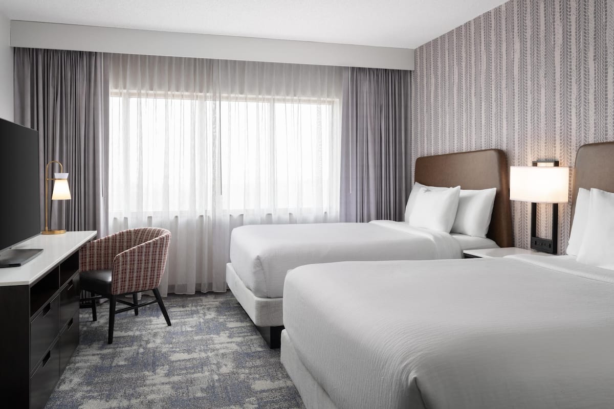 Une chambre d’hôtel avec deux lits, un bureau, une chaise et un téléviseur.
