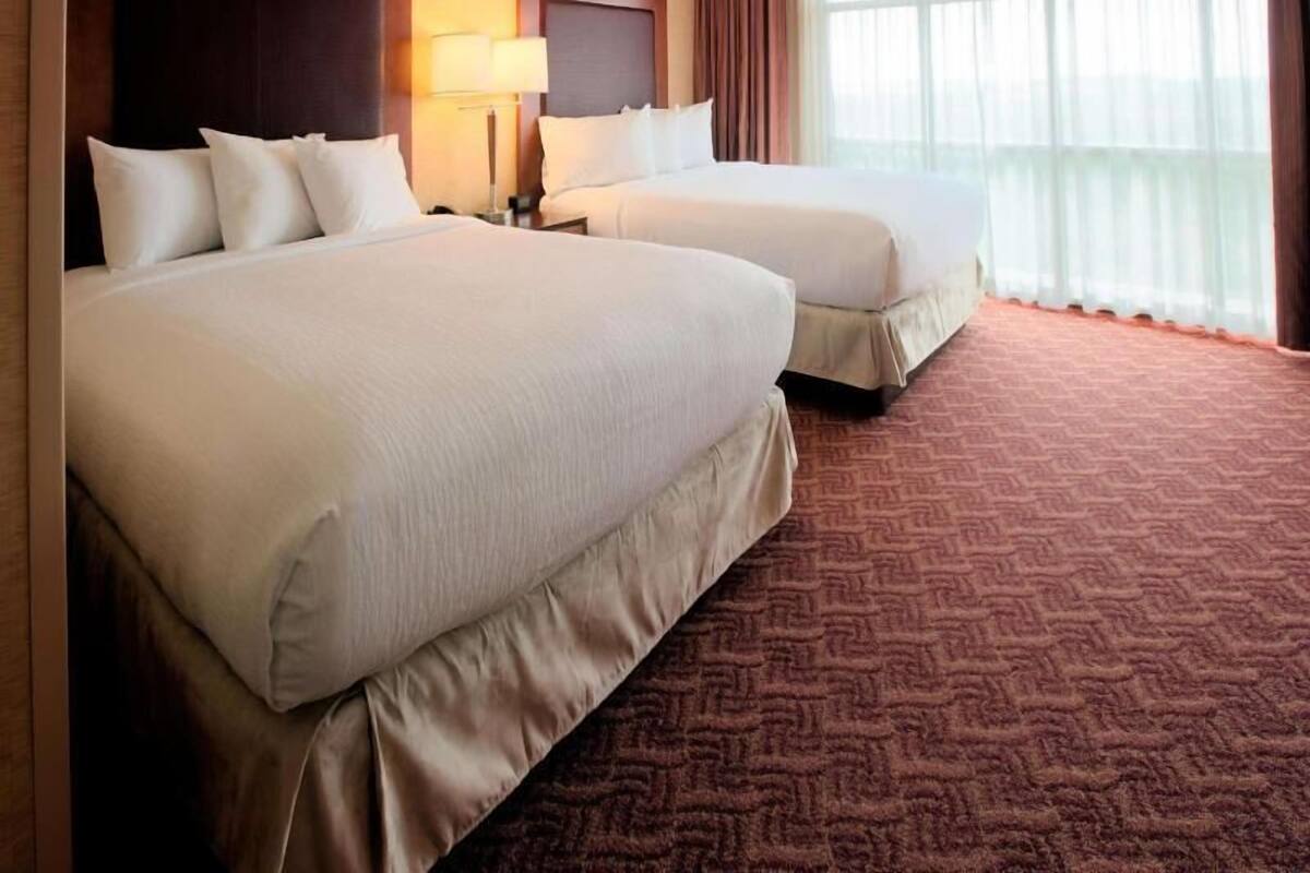 Een hotelkamer met twee bedden, een hoofdeinde, een nachtkastje, een lamp en een raam met gordijnen.